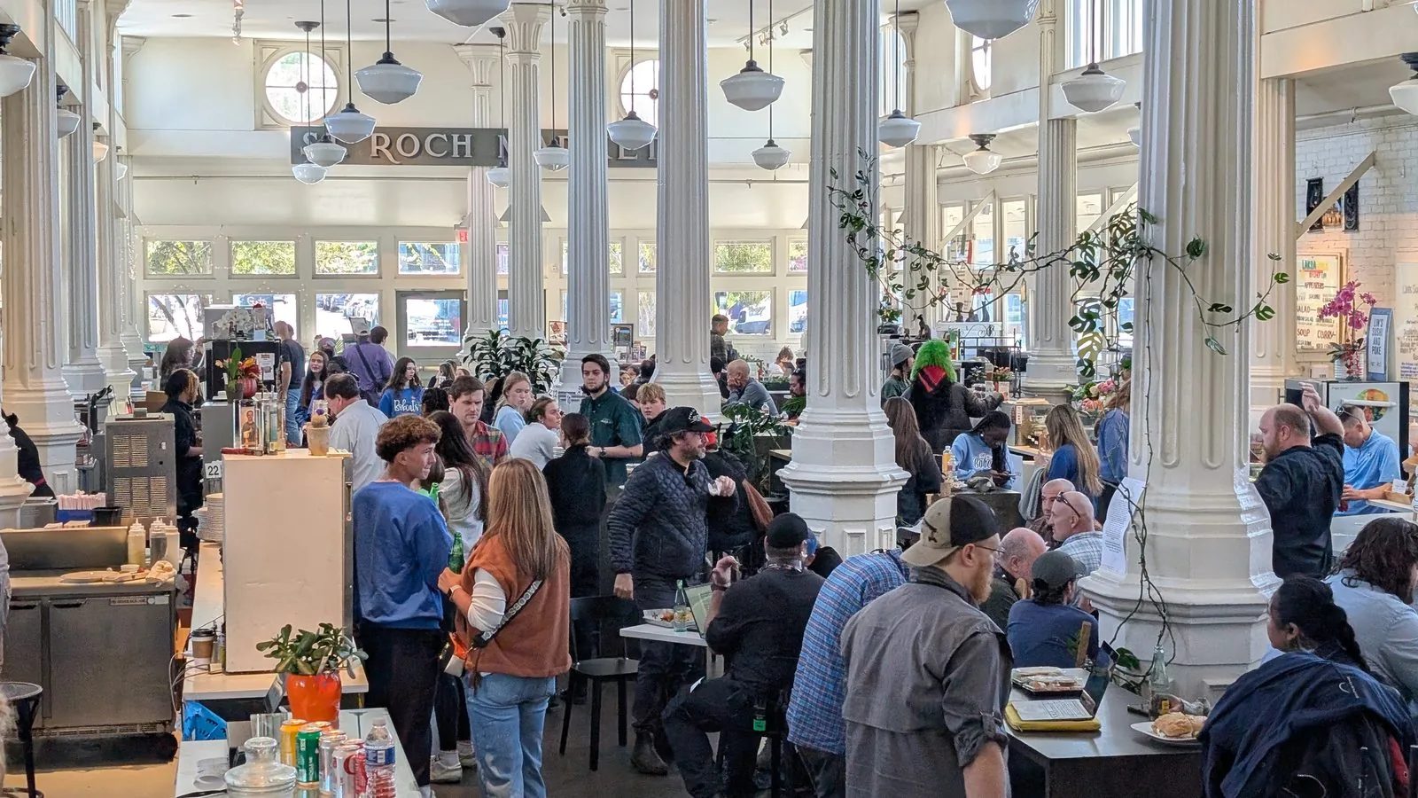 A busy evening inside St. Roch Market New Orleans food hall with guests dining between historic white cast iron columns