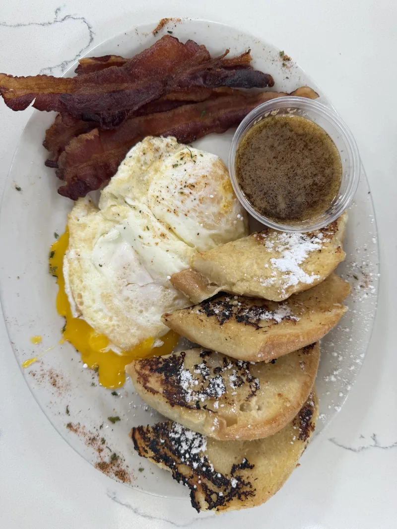 French toast at Chef Charles Bistreaux, dusted with powdered sugar and served with bacon, eggs, and cane syrup