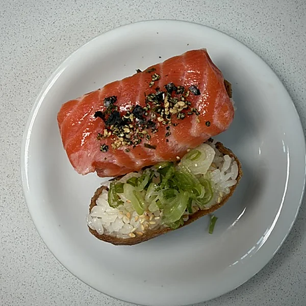 Two inari at Lin's Poke & Sushi, one topped with a slab of salmon and nori goma, the other with sushi rice, sliced scallions, and sesame seeds