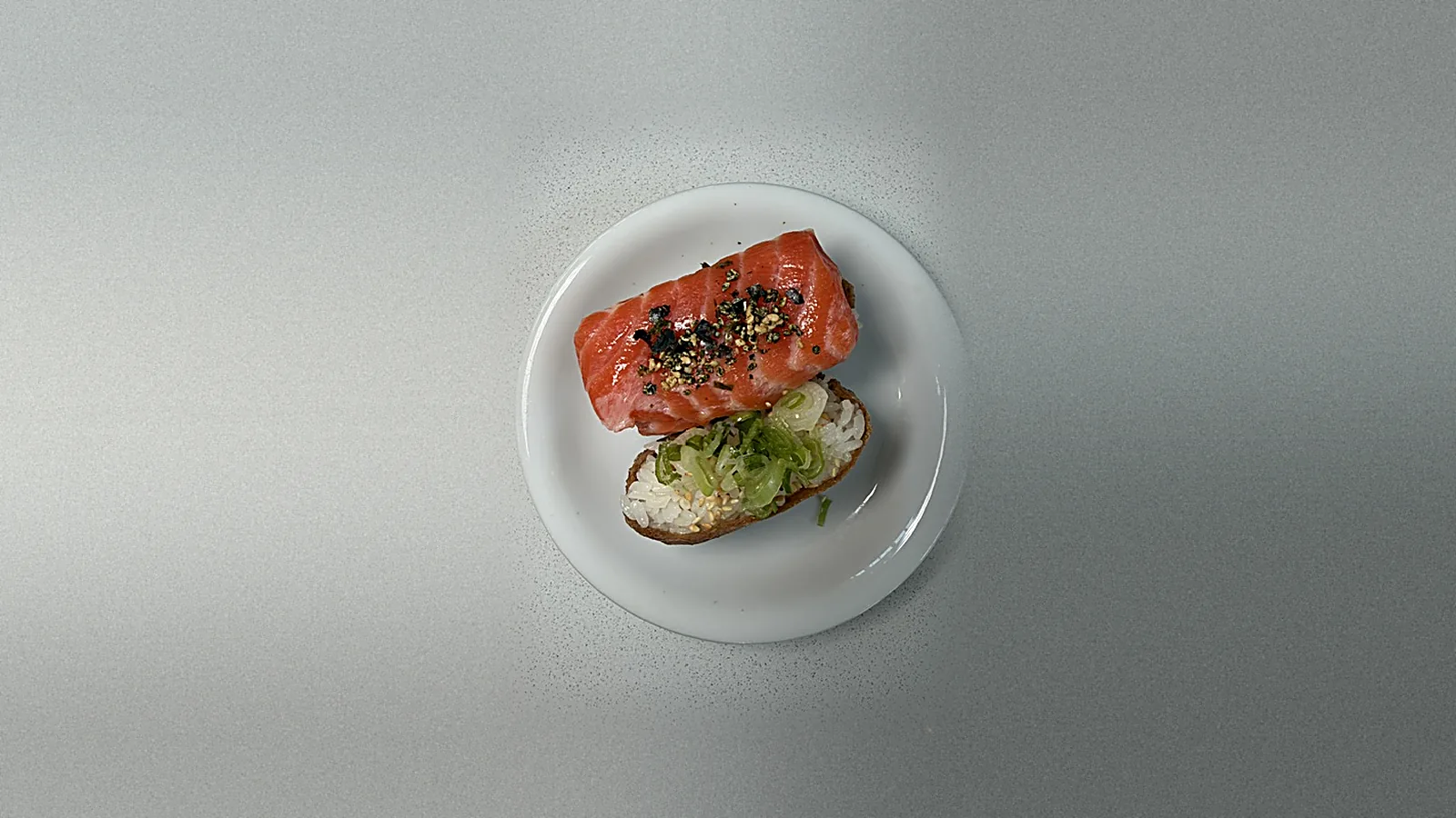 A salmon-topped inari and a rice-only inari on a white plate at Lin's Poke & Sushi: fried tofu pockets filled with sushi rice, one draped with a thick slab of salmon and sprinkled with nori goma, the other piled with sliced scallions and sesame seeds