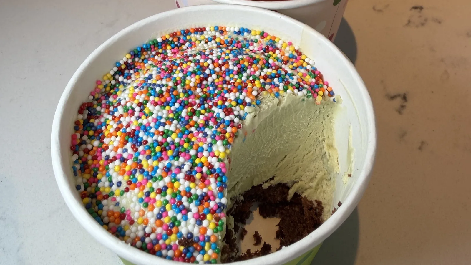 A Dubai Chocolate Pistachio dot cake at Olive & Co, cut open to show pistachio frosting and chocolate cake under a dome of rainbow sprinkles