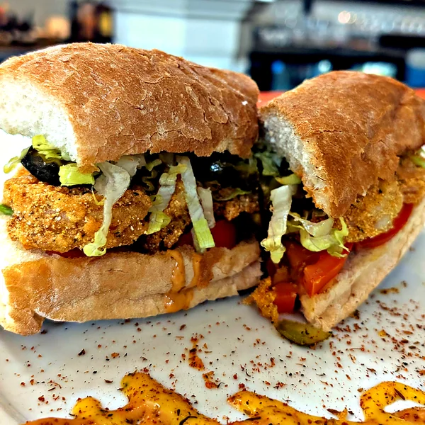 A fried oyster po-boy cut in half on a white plate at Salted Pearl Oyster Bar, cornmeal-crusted oysters with shredded lettuce and tomato on French bread