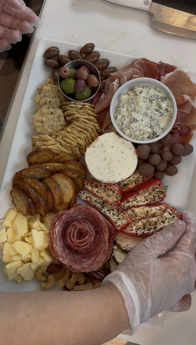 A prep plate at Olive and Co with stuffed peppers, a salami rose, and a gloved hand plating charcuterie at St. Roch Market